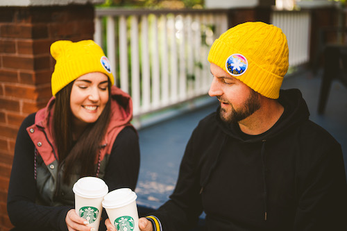man and woman sitting on porch drinking starbucks and wearing CNOY toques